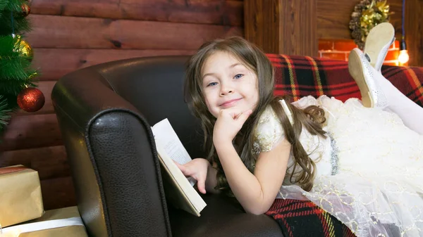 Uma criança lê um livro interessante na árvore de Natal . — Fotografia de Stock