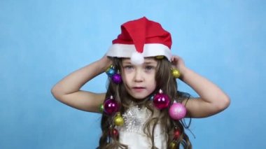 Çocuk kafasına yeni yıl şapkası takıyor. Saçında Noel topları olan bir kız kafasına kırmızı bir şapka takıyor..