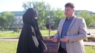 Beyaz adam ve İslami kadın sokakta sohbet ediyorlar. Avrupalı yetişkin bir adam, ulusal kıyafetli Müslüman kız arkadaşına komik bir hikaye anlatıyor..