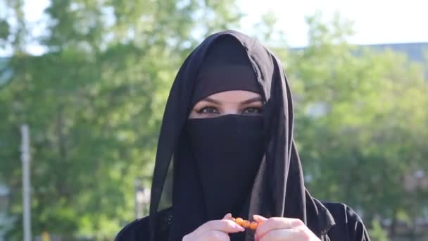 イスラム教徒の女性はバラ色のイスラムのスコアで立っている 民族衣装を着たイスラム教徒の女性は手に宗教的なロザリオを持っています — ストック動画