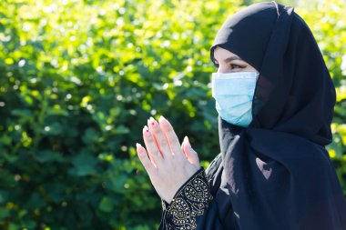Koruyucu tıbbi maskeli Müslüman kadın Tanrı 'ya dua ediyor. Tıbbi maskeli Müslüman kadın kendini tecrit ve virüs karantinası sırasında sokakta namaz kılıyor.