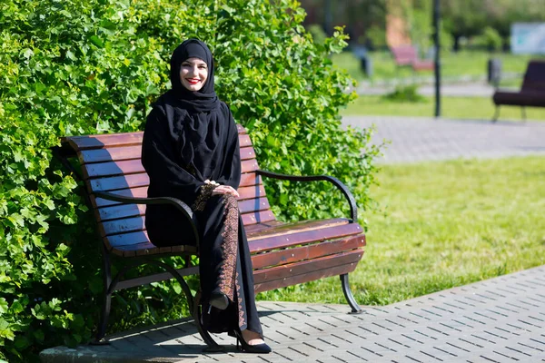 美しい若いイスラム教徒の女性がベンチに座っています 公園のベンチに腰を下ろして — ストック写真