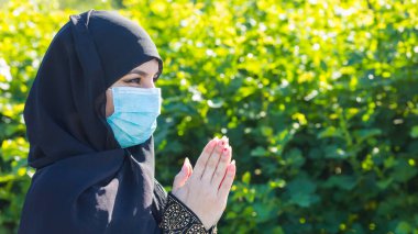 Koruyucu tıbbi maskeli Müslüman kadın Tanrı 'ya dua ediyor. Tıbbi maskeli Müslüman kadın kendini tecrit ve virüs karantinası sırasında sokakta namaz kılıyor