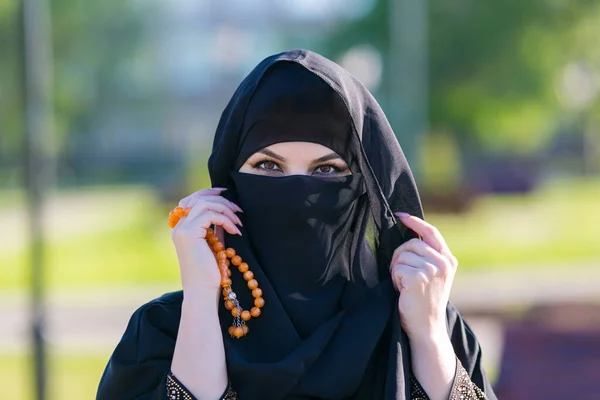 Muslim woman stands with rosary Islamic scores. Islamic woman in national women\'s clothing holds religious rosary in her hands.