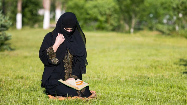 市内公園でのイスラム教徒の女性の祈り イスラム教徒の女性は公園で緑の草の上に座って朝の祈りを実行します — ストック写真