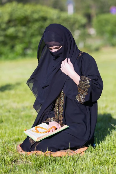 イスラム教徒の女性は緑の芝生の公園に座って朝の祈りを実行します 都市公園でのイスラム教徒の女性の祈り — ストック写真