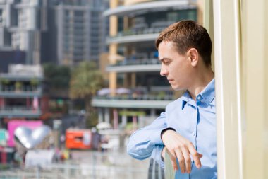 Şehrin balkonundan bir adam bakıyor. 35-40 yaşlarında beyaz bir adam balkonda duruyor ve şehir hayatına bakıyor..