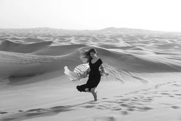 Running woman in the desert. Black and white image Cheerful young girl with long hair in the desert of Dubai.