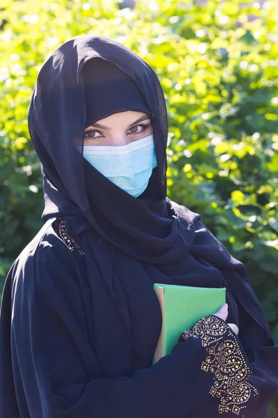 顔に描かれた仮面の中近東からの移住者は 木を背景に緑を手にしている 手の中に保護医療マスククォーンの東洋の女性 — ストック写真
