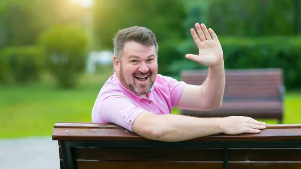 40-45 yaşlarında pembe tişörtlü beyaz bir adam elini sımsıkı sallıyor ve geniş bir şekilde gülümsüyor. Gri saçlı mutlu yetişkin adam elini sallıyor..