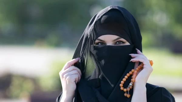 A migrant woman from the east in black clothes. A woman from the east in national Islamic clothes holds religious supplies her hands.