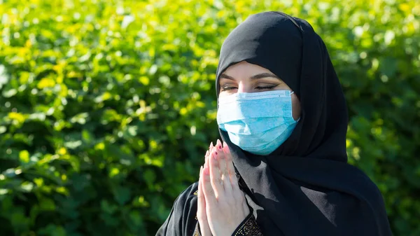 Muslim girl in a protective medical mask prays to God during self-isolation and viral quarantine