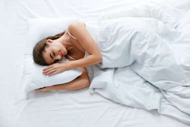 Sağlıklı uyku. Beyaz yatak takımları, yumuşak yastık, battaniye ile yatak üzerinde uyuyan kadın. Yüksek çözünürlük.