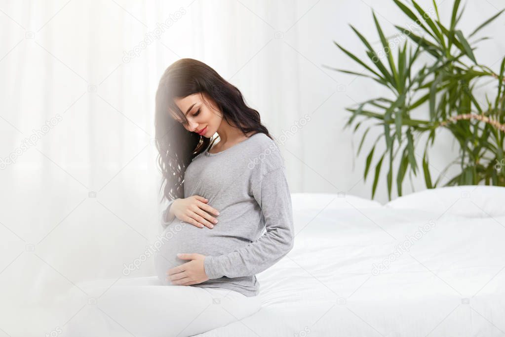 Pregnant Women. Beautiful Happy Pregnant Woman With Belly Sitting On Bed Indoors. High Resolution