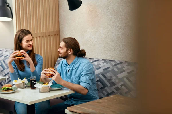 Couple With Burgers. Man And Woman Eating Fast Food In Cafe. High Resolution.