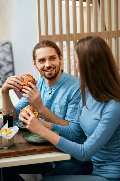Couple With Burgers. Man And Woman Eating Fast Food In Cafe. High Resolution.