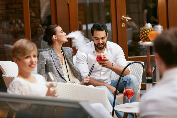 People Smoking Shisha, Drinking Cocktails In Hookah Bar. Couple Smoke And Drink In Restaurant. High Resolution