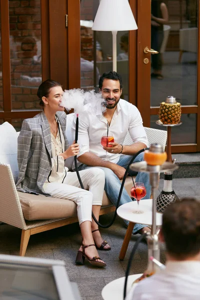 Couple Smoking Shisha And Drinking Cocktails In Hookah Bar. Man And Woman Relaxing In Cafe. High Resolution
