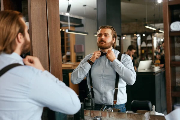 Man Dressing Up Near Mirror In Salon. Portrait Of Handsome Male Barber Tying Bow Tie. High Resolution