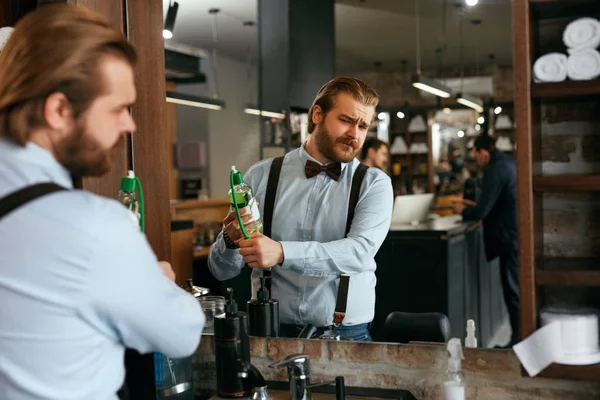 Handsome Man Using Perfume Spray In Barber Shop. Portrait Of Male Spraying Cologne Near Mirror In Hair Salon. High Resolution