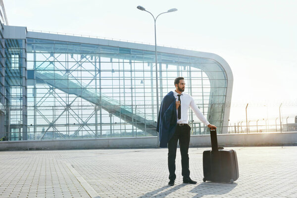 Деловой человек путешествует по делам. Красавчик в костюме с чемоданом собирается в аэропорт. Высокое разрешение
