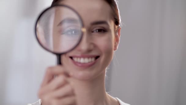 Kobieta, patrząc przez szkło powiększające i uśmiechnięty Close Up — Wideo stockowe