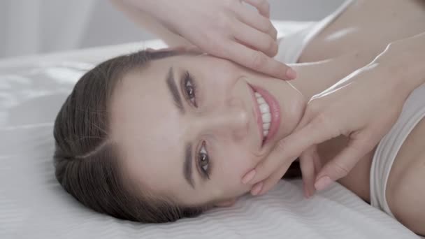 Cuidado facial. Mujer joven acostada en la cama y tocando la piel en la cara — Vídeo de stock