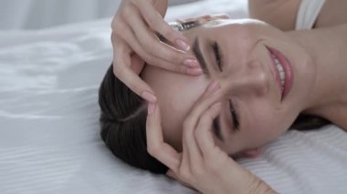 Yüz bakımı. Yatakta yatarken ve yüzünde cilt dokunmadan genç kadın