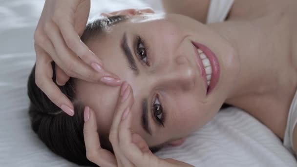 Cura del viso. Giovane donna sdraiata sul letto e toccando la pelle sul viso — Video Stock