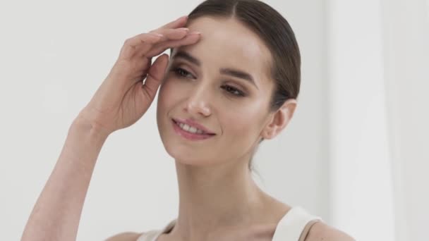 Догляд за красою. Приваблива усміхнена жінка пестить шкіру обличчя — стокове відео