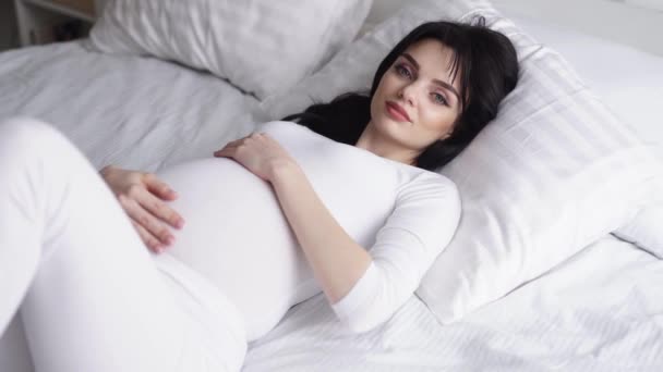 Enceinte belle femme allongée sur le lit et caressant ventre de bébé — Video