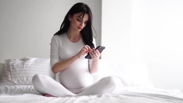 Zwangere aantrekkelijke vrouw met behulp van mobiele telefoon op Bed — Stockvideo