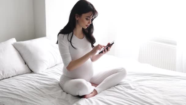 Těhotná žena atraktivní pomocí mobilního telefonu na postel — Stock video