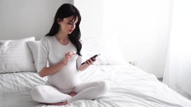 Mulher atraente grávida usando telefone celular na cama — Vídeo de Stock