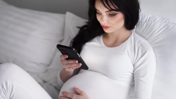 Беременная привлекательная женщина с помощью мобильного телефона на кровати — стоковое видео