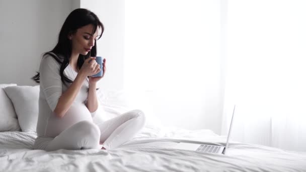Kobieta w ciąży picia herbaty, za pomocą komputera w domu w sypialni — Wideo stockowe