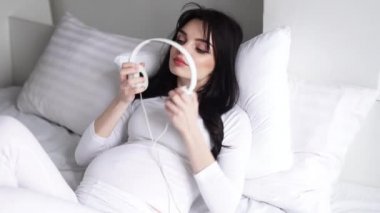 Hamile kadın dinleme müzik kulaklık ve yatak üzerinde oturan