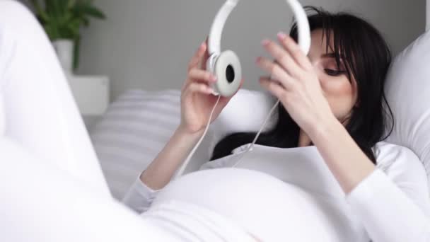 임신 한 여자가 벨리에서 헤드폰으로 임신 음악을 듣는 모습 — 비디오