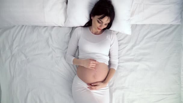 Mulher grávida tocando barriga do bebê e deitado na cama em casa — Vídeo de Stock