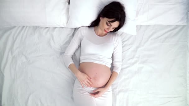 妊娠中の女性の赤ちゃんお腹に触れると自宅のベッドに横になっています。 — ストック動画