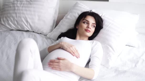 Gravidez. Mulher bonita deitada na cama e tocando barriga do bebê — Vídeo de Stock