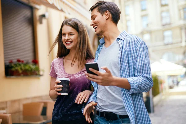 Пара с помощью мобильного телефона и питьевой кофе на открытом воздухе — стоковое фото