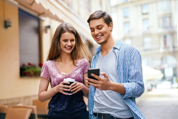 Casal usando telefone celular e beber café ao ar livre — Fotografia de Stock