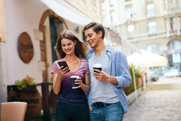 Paar met behulp van de mobiele telefoon en het drinken van koffie buitenshuis — Stockfoto