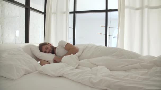Człowiek, który śpi w łóżku z białą pościelą w sypialni światło — Wideo stockowe