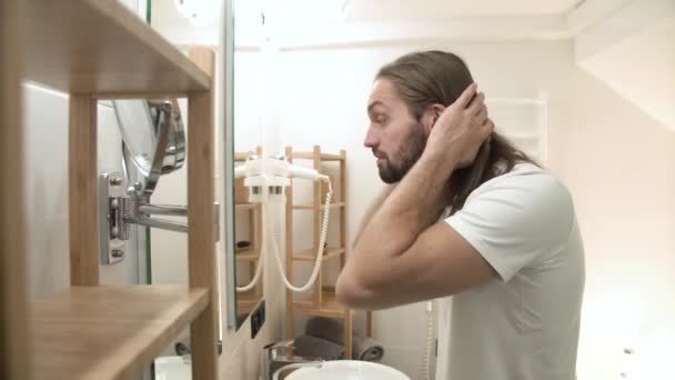 Mann im Badezimmer blickt in Spiegel und berührt Gesicht — Stockvideo