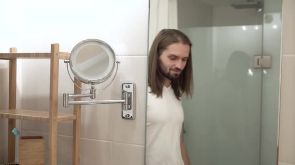 Mann im Badezimmer blickt in Spiegel und berührt Gesicht — Stockvideo