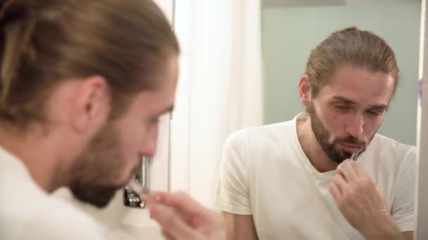 Man tanden poetsen en kijken naar spiegel in de badkamer — Stockvideo