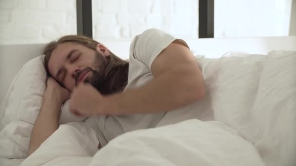 Man sover, vaknar upp morgonen i sängen med vita sängkläder — Stockvideo