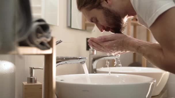 Утренняя гигиена. Мужчина, умывающий лицо чистой водой в ванной — стоковое видео
